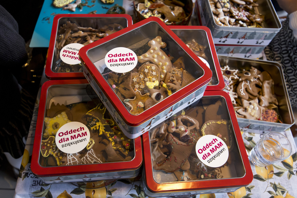 Metalowe puszki z naklejką „Oddech dla Mam. Dziękujemy!” wypełnione udekorowanymi piernikami stoją ułożone jedna na drugiej na stole.